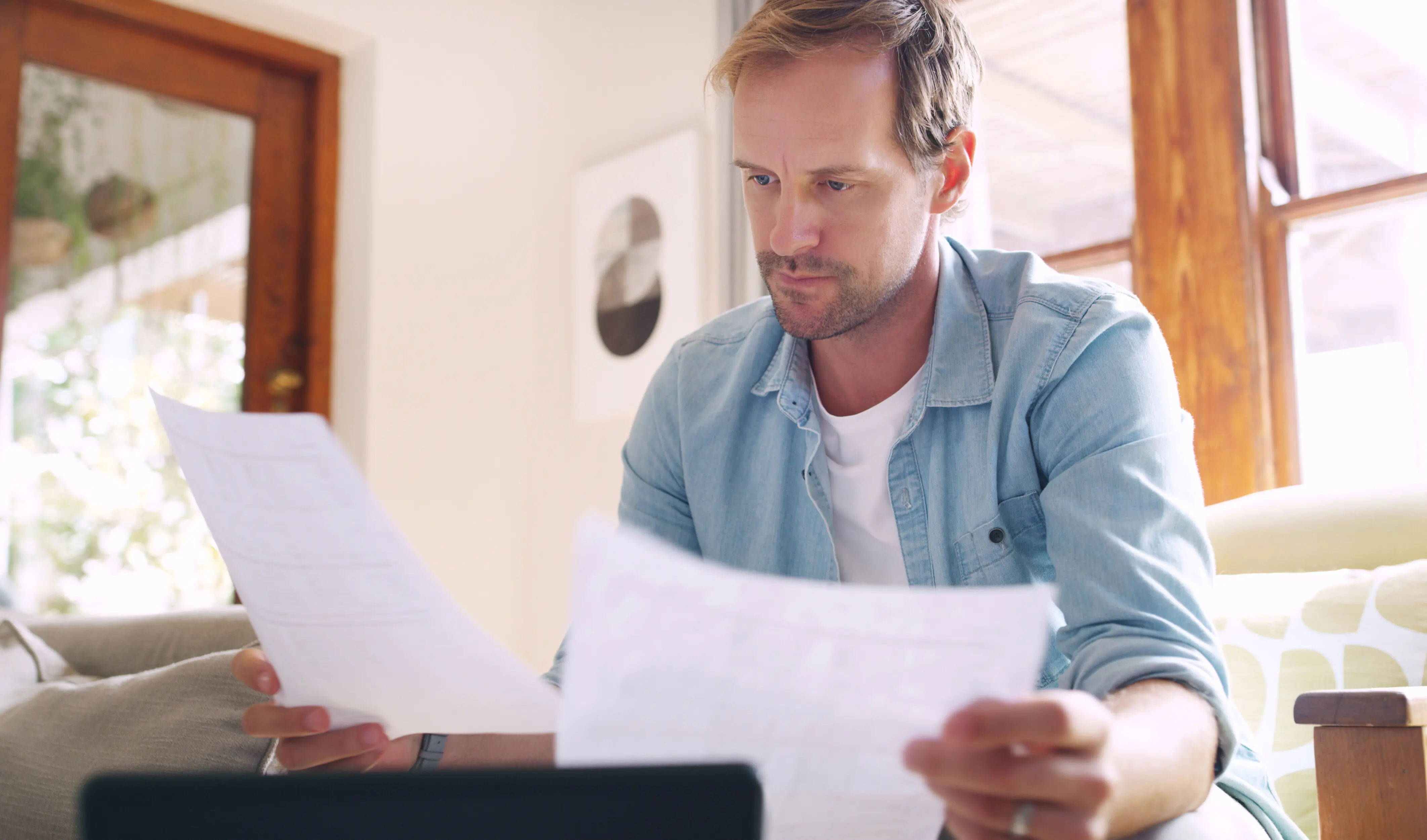 A man at home, thinking and relaxing with documents and a tablet, dealing with financial bankruptcy or mortgage debt payments, reading and handling paperwork for a budget crisis, an eviction letter, and an investment solution.